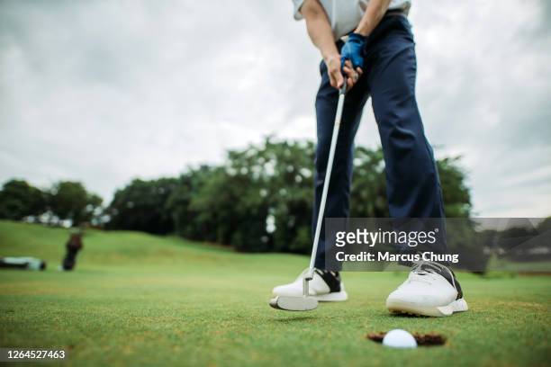disparo de cosecha de asiático chino joven golfista masculino tocando la pelota de golf en un agujero en el campo de golf - golf sport fotografías e imágenes de stock