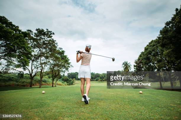 vista posteriore della giovane golfista cinese asiatica che teeing off e swing il suo club di autisti sul campo da golf - woman on swing foto e immagini stock