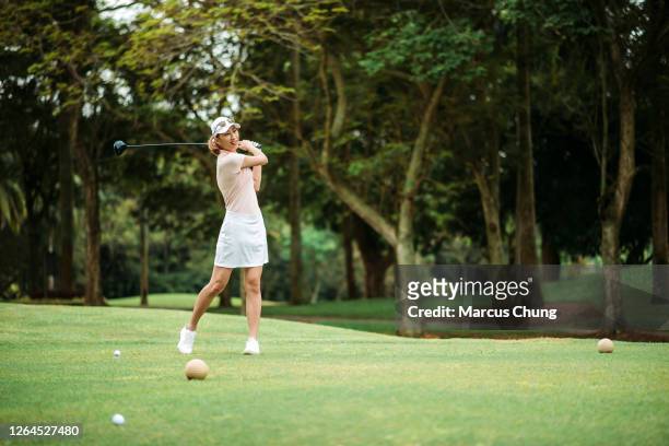 asian chinese smiling young female golfer teeing off and swing her driver club on the golf course - golf driver stock pictures, royalty-free photos & images