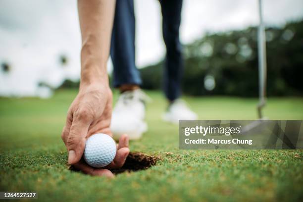 sluit omhoog van aziatische chinese jonge mannelijke golfer die golfbal met hand bij het gat van golfcursus oppakt - golfclub stockfoto's en -beelden