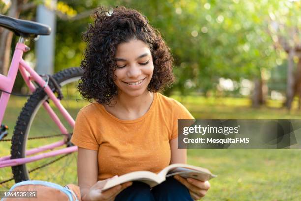 teen girl reading book in the park - children's literature stock pictures, royalty-free photos & images