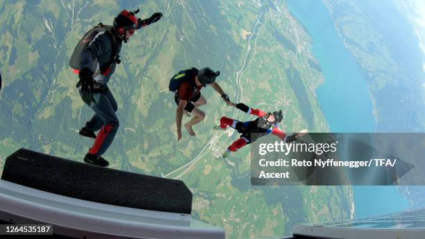 wingsuit fliers launch themselves out of an airplane high above a lush valley and lake - leap of faith activity stock pictures, royalty-free photos & images