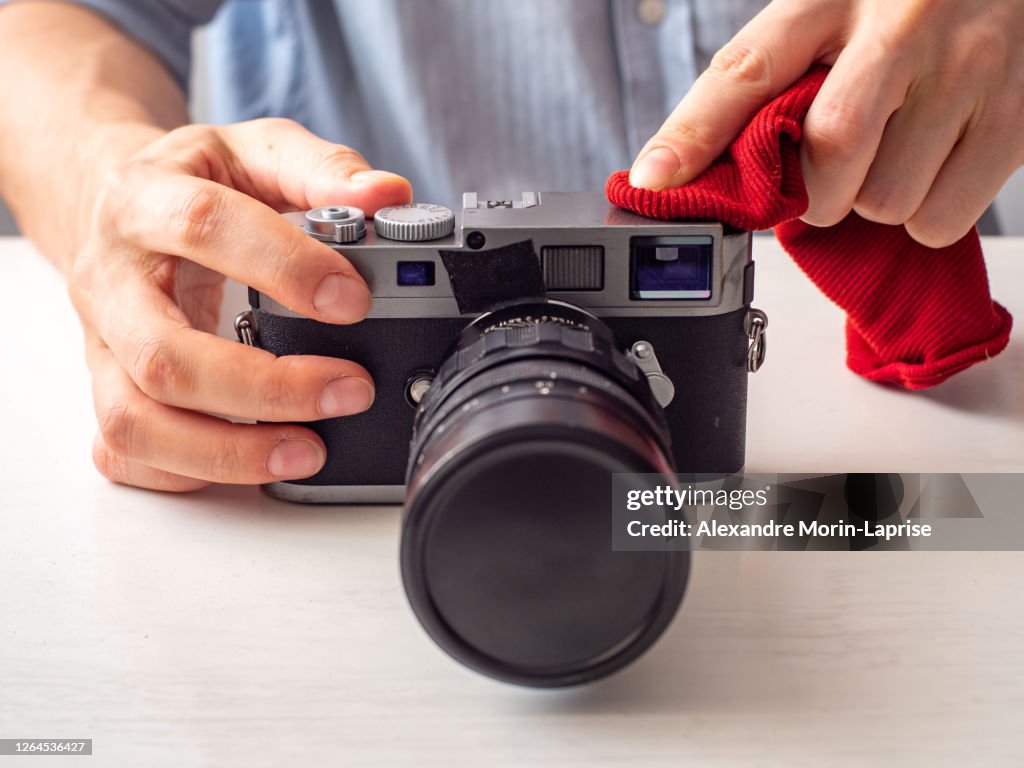 Caucasian Man Cleans Vintage Old School Looking Range Finder Camera with a Red Piece of Cloth on a White Table