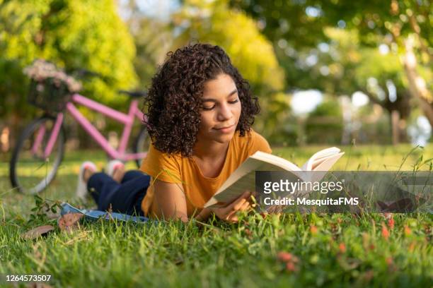 tenn meisje dat een boek leest dat op het gras ligt - reading stockfoto's en -beelden