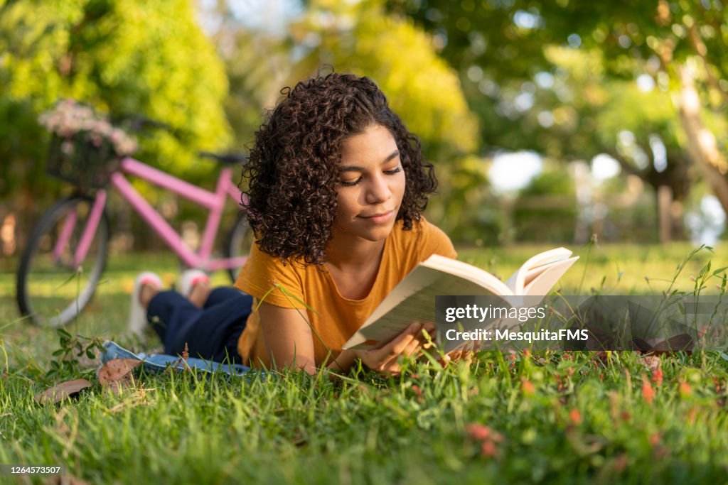 Tenn girl reading a book lying on the grass