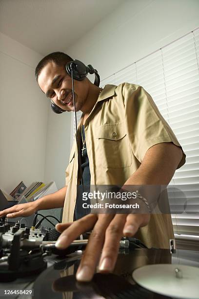 asian young adult male dj standing with hand on spinning record on turntable and smiling. - record scratching stock pictures, royalty-free photos & images