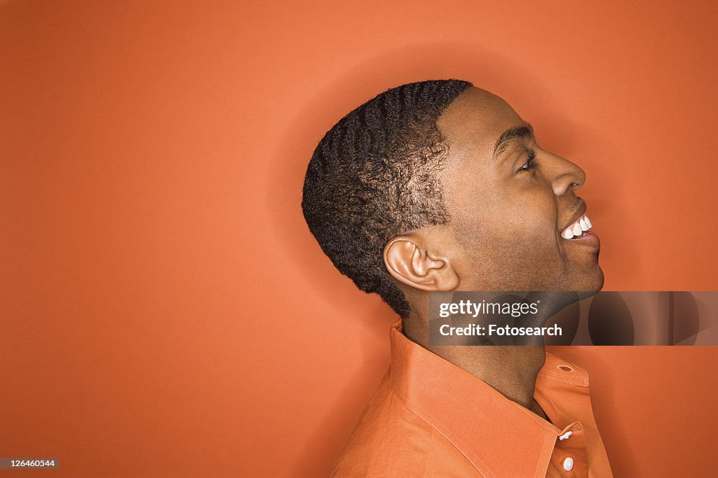 Side view of smiling young African-American man on orange background.