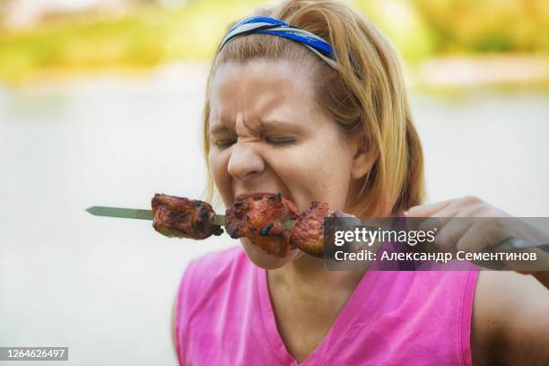 a woman eats meat cooked over an open fire. the summer bank of the river. - chewing with mouth open stock pictures, royalty-free photos & images