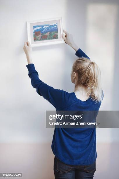 blond woman hanging picture to the wall - adjusting bildbanksfoton och bilder