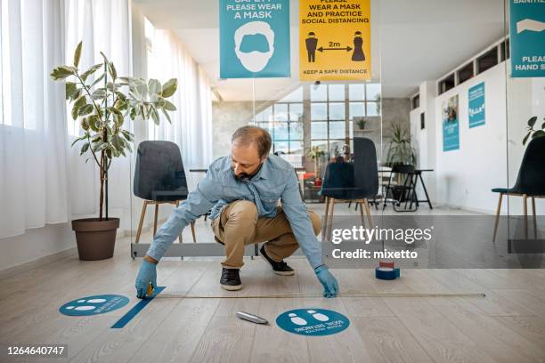 hombre aplicando cartel de distanciamiento social en la oficina - social distancing fotografías e imágenes de stock