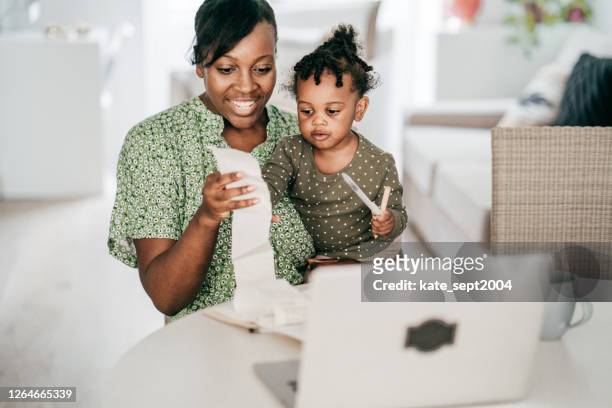 organizing family finances -mom with baby sitting in front of computer while holding receipt - financial wellbeing stock pictures, royalty-free photos & images