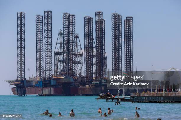 Groups of people relax in the sun of the Caspian Sea in front of oil rigs following the easing of strict quarantine measures against the spread of...