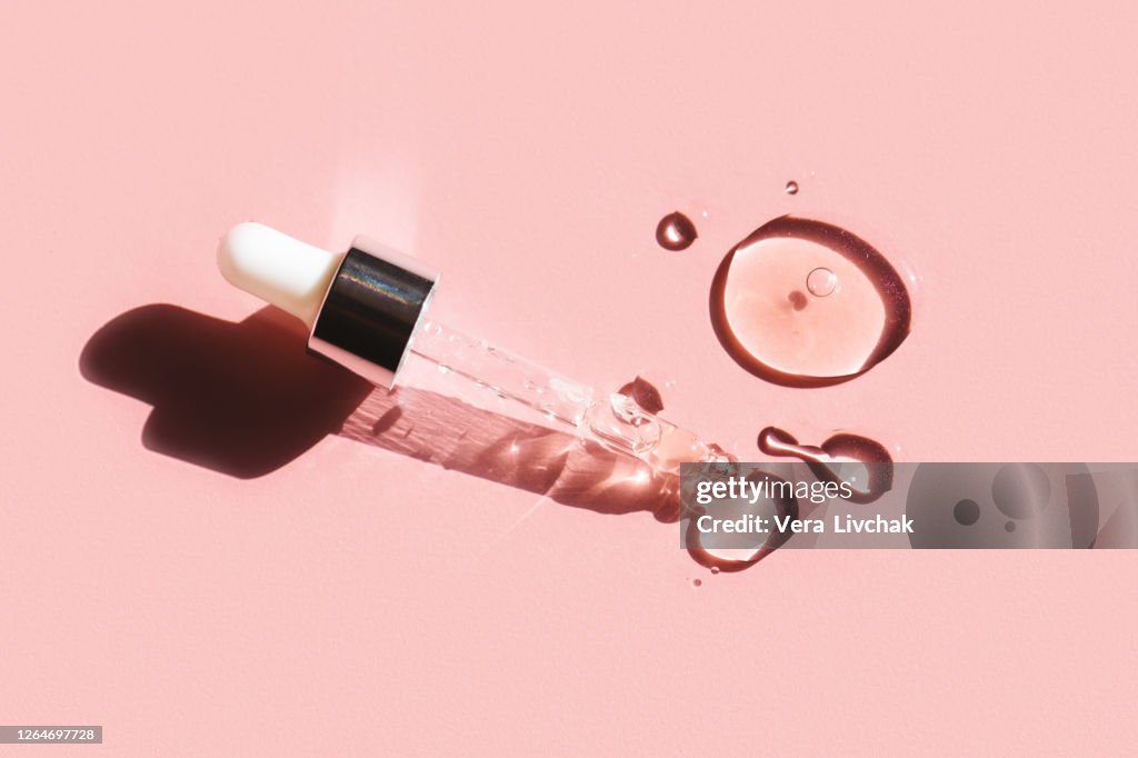 Flat lay. Liquid gel or serum drop with pipette on pink background in macro.