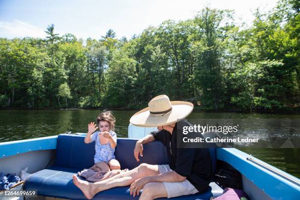 3 year old girl swiping iphone while seated in a motorboat with adult in large sunhat seated next to her. - wide brim stock-fotos und bilder