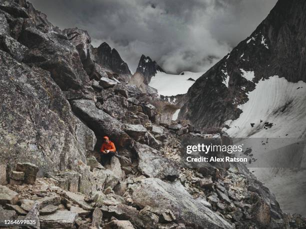 rock climber takes cover under a boulder during dramatic thunderstorm on a tall, rock spire in bugaboo glacier provincial park - ominous mountains stock pictures, royalty-free photos & images