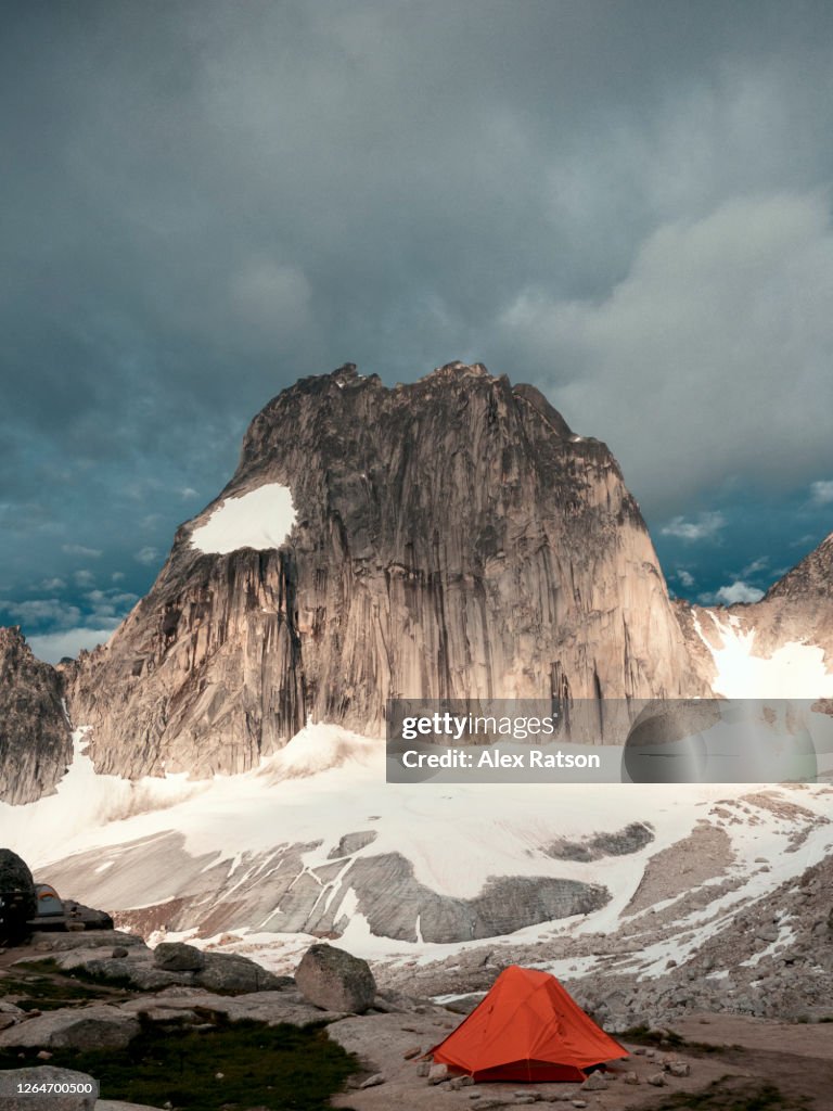 Orange tent beneath Snowpatch Spire at sunrise on a overcast day in Bugaboo Glacier Provincial Park