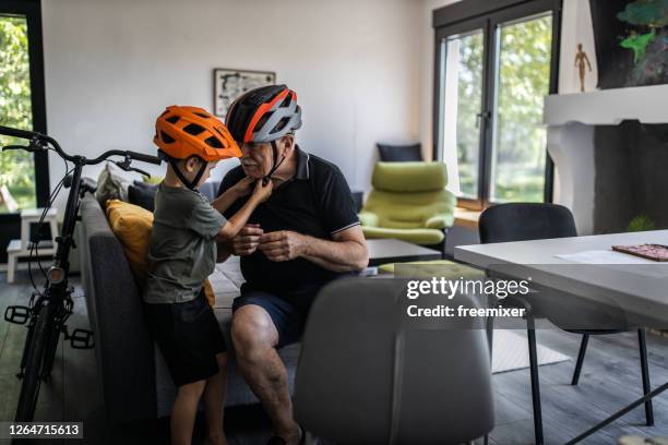 grandfather and grandson sitting in living room and fitting cycling helmets - sports helmet stock pictures, royalty-free photos & images