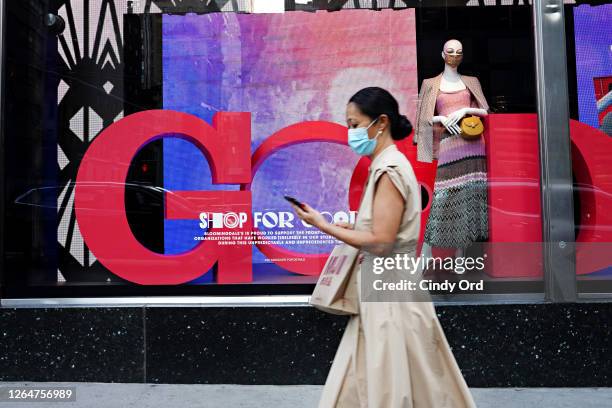 Woman wearing a protective mask walks by a store window display featuring a mannequin wearing a protective mask as the city continues Phase 4 of...