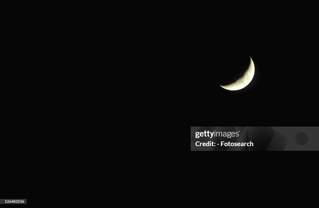 A crescent moon against a black starless sky