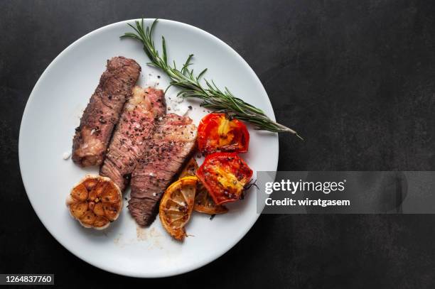 sliced grilled wagyu steak served on white plate with grilled sliced lemon, tomatoes, garlic and rosemary. - steak plate stock pictures, royalty-free photos & images