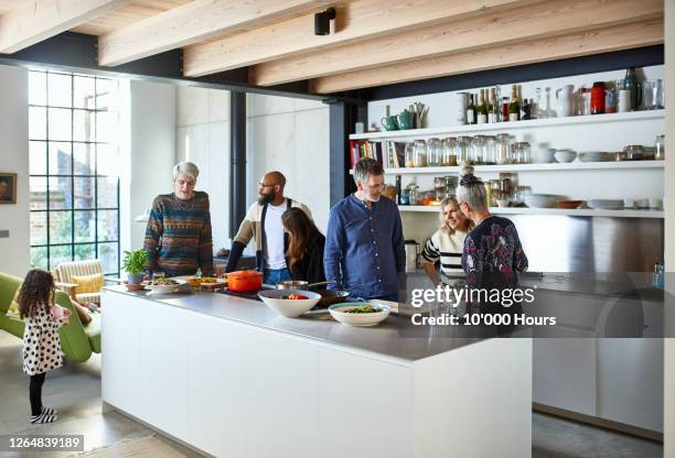friends gathering in open plan kitchen for lunch - generationen kochen stock-fotos und bilder