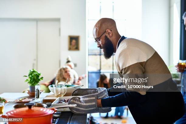 mid adult man making dinner wearing oven gloves - victory dinner stockfoto's en -beelden