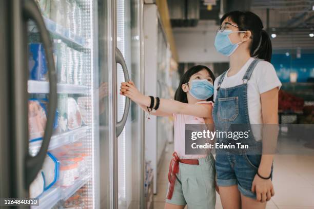 an asian chinese young girl looking at the refrigerated section choosing for her ice cream with her sister - fridge handle stock pictures, royalty-free photos & images