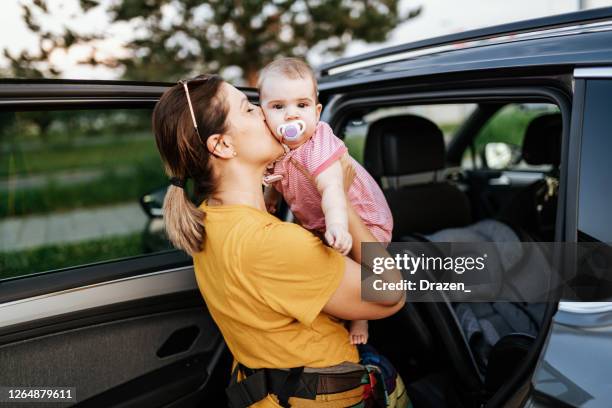 kvinna sätter barnet i bilbarnstol och spänn säkerhetsbältet. baby är glad och älskvärd. - baby bag bildbanksfoton och bilder