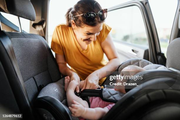 donna che mette il bambino sul seggiolino e fissa la cintura di sicurezza. il bambino è allegro e amabile. - child car seat foto e immagini stock