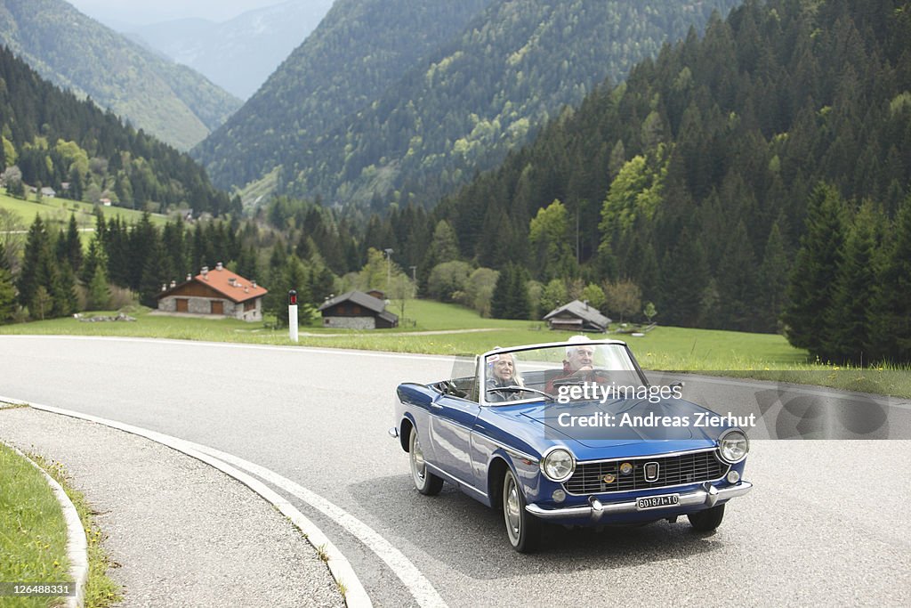 Senior couple driving convertible on country road, Italy