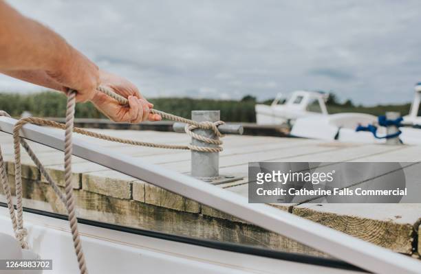 man securing a rope to a boat cleat - anlegetau stock-fotos und bilder