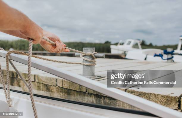 man securing a rope to a boat cleat - amarre fotografías e imágenes de stock