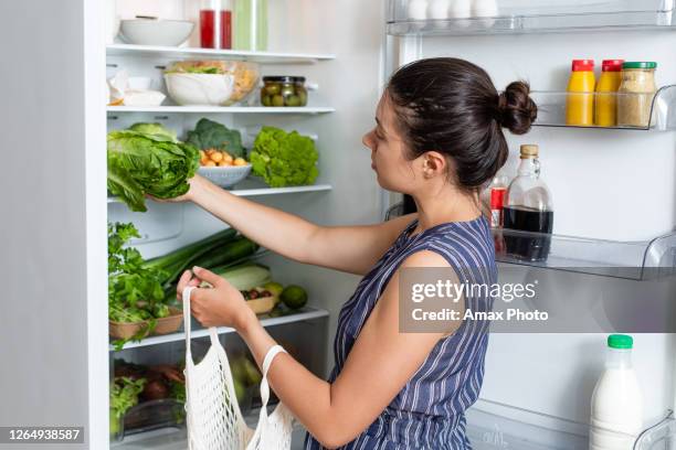 frau mit eco-tasche legt gemüse in den kühlschrank. lebensmittel-lebensmittel-korb. kunststofffrei, null abfall, umweltfreundliches konzept. - full figure stock-fotos und bilder