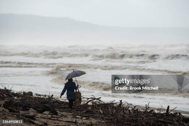 Woman walks through the charred debris of the Black Summer bushfires which have been washed onto the beach after the Shoalhaven River flooded on...