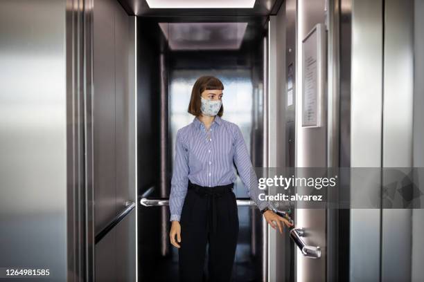 female wearing face mask using elevator in office - social distancing elevator stock pictures, royalty-free photos & images
