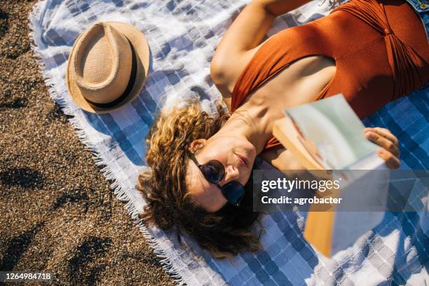 mulher deita na praia lendo um livro - women sunbathing - fotografias e filmes do acervo