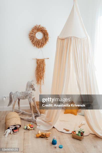 messy children's playroom full of toys. beautiful decoration nursery with natural macrame decoration, organic canopy, wicker baskets and wood toys. vertical photo. - baby room stock pictures, royalty-free photos & images
