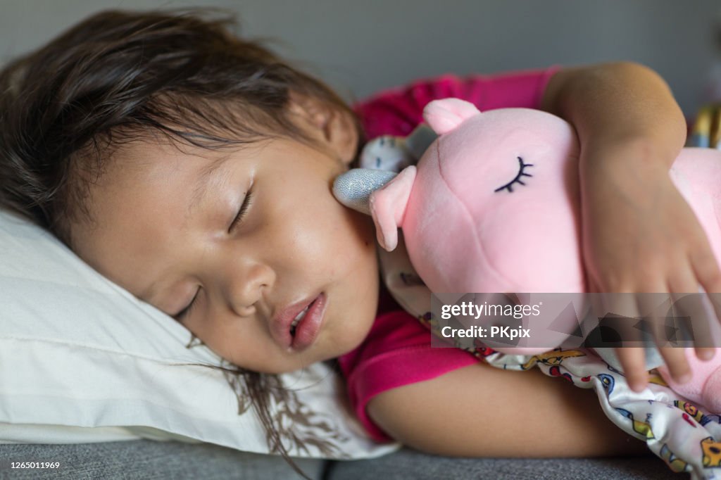 Söt sovande liten asiatisk flicka småbarn i sängen medan kramar en gose- leksak.