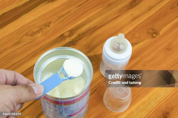 new parents powder milk and blue spoon on light background close-up. milk powder for baby in measuring spoon on can. powdered milk with spoon for baby. baby milk formula and baby bottles. - milchpulver stock-fotos und bilder