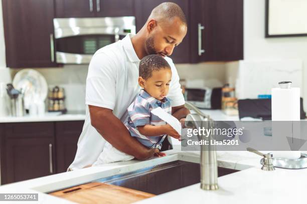 afroamerikanischer vater hilft seinem sohn, seine hände zu waschen - küchenrollenpapier stock-fotos und bilder