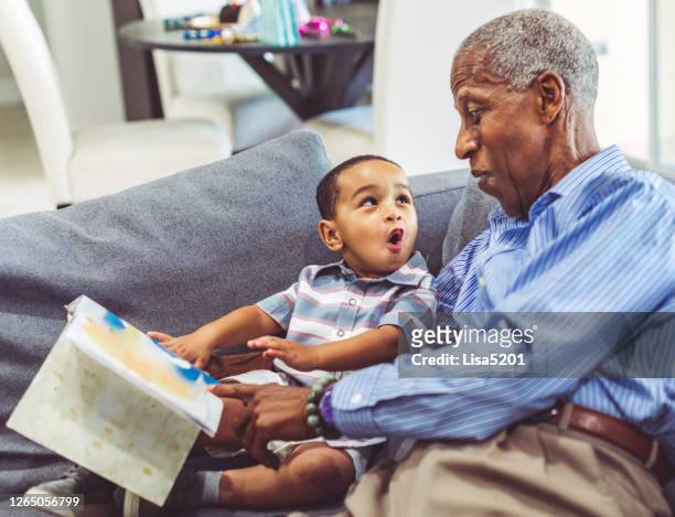african american grandchild and grandfather read a book together at home - grandfather stock pictures, royalty-free photos & images