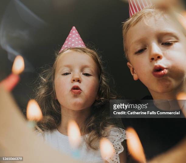 two young kids blowing out birthday candles - pusten stock-fotos und bilder