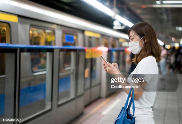 asian woman texting at the metro station wearing a facemask - emergency response stock pictures, royalty-free photos & images
