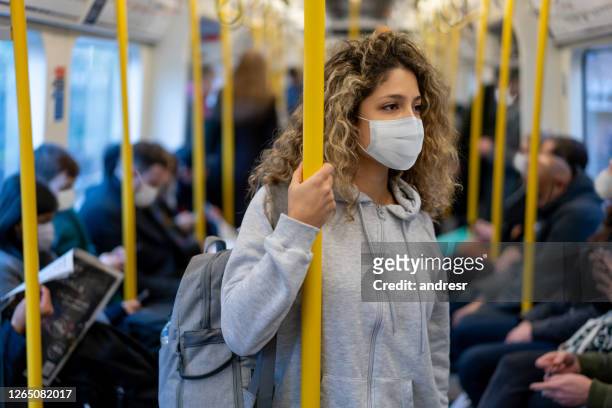 donna in sella alla metropolitana che indossa una maschera facciale per evitare una malattia infettiva - protective face mask foto e immagini stock