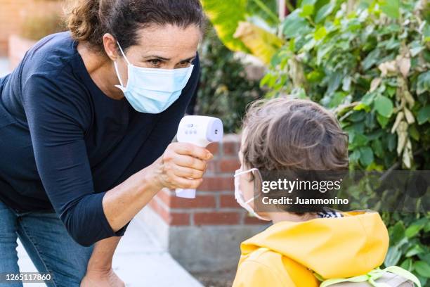 school teacher taking temperature to a little child boy before he goes back to school - bubonic plague mask stock pictures, royalty-free photos & images