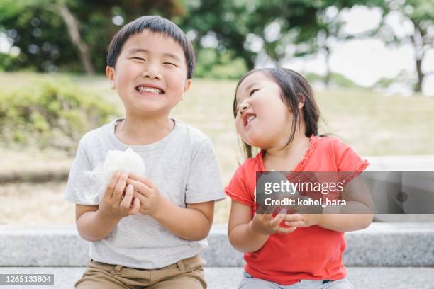 geschwister essen reiskugel im park - cute japanese boy stock-fotos und bilder