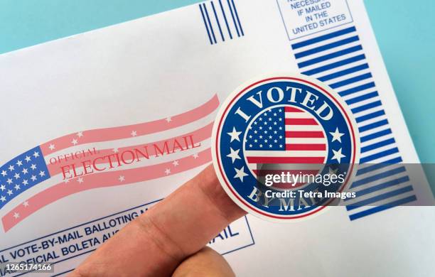 human finger holding sticker above voting mail - voting by mail stockfoto's en -beelden