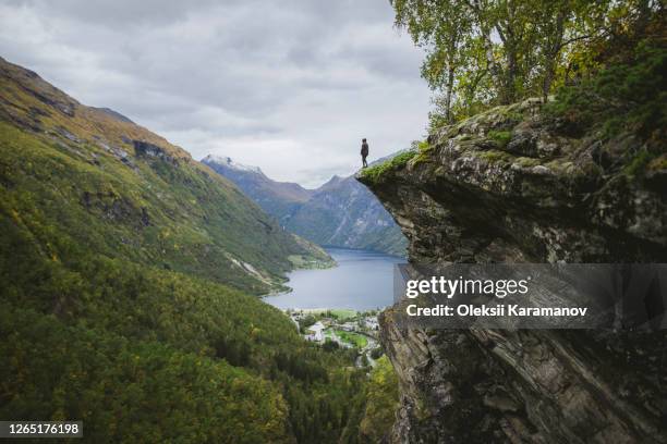 norway, geiranger, man standing on edge of steep cliff above geirangerfjord - geiranger stock-fotos und bilder