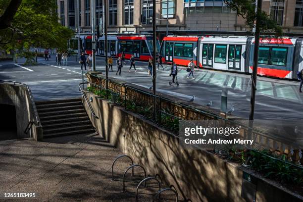 city street with red tram, lightrail and people social distancing on footpath - lightrail stock pictures, royalty-free photos & images