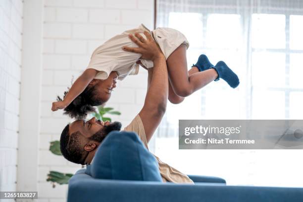 african father picking up daughter in the air, face to face. they are having fun in weekend at home. - life insurance stockfoto's en -beelden